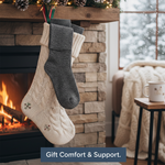 A pair of stylish compression socks peeking from a holiday stocking by a fireplace, representing "The Ultimate Stocking Stuffer" for comfort and support. Shows a thoughtful, practical gift.
